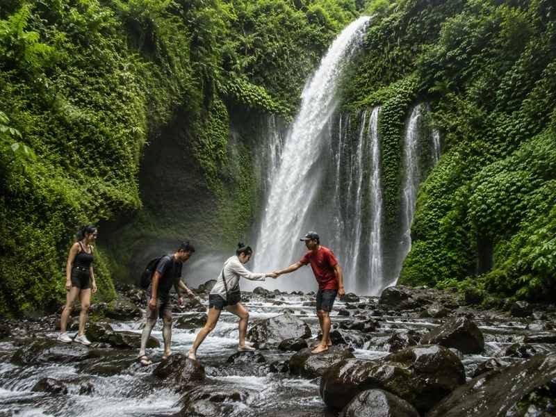 Local guide helping guests cross wet rocks at Tiu Kelep Waterfall